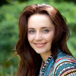 A woman with long red hair and a colorful shirt.