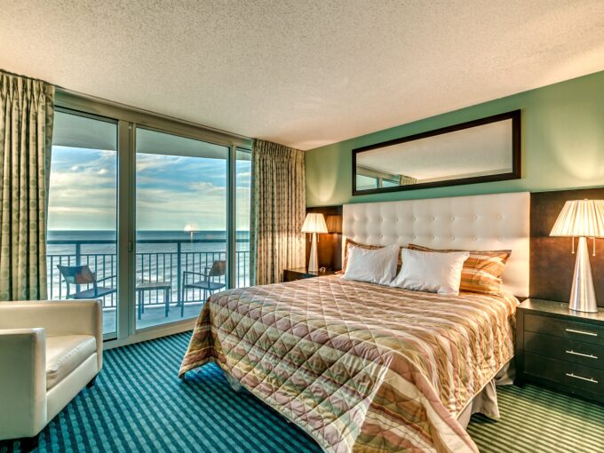 A bedroom with a large bed and balcony overlooking the ocean.