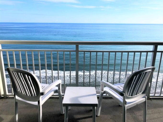 Two chairs and a table on the balcony of an ocean front hotel.