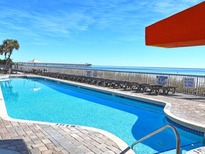 A pool with an umbrella and chairs on the side of it.