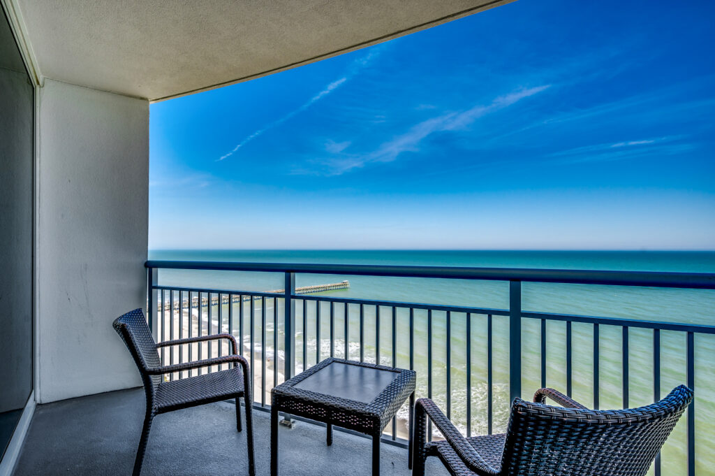 A balcony with chairs and tables overlooking the ocean.