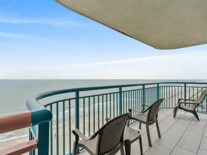 A balcony with chairs and tables overlooking the ocean.