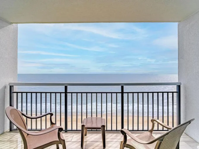 A balcony with chairs and tables overlooking the ocean.