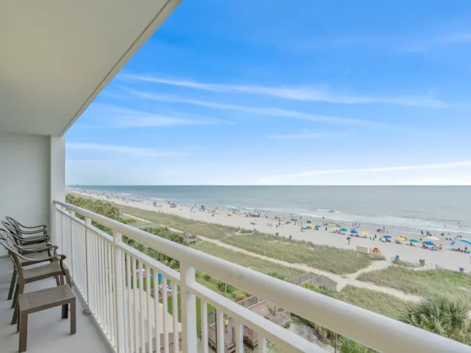 A balcony with chairs and tables overlooking the beach.