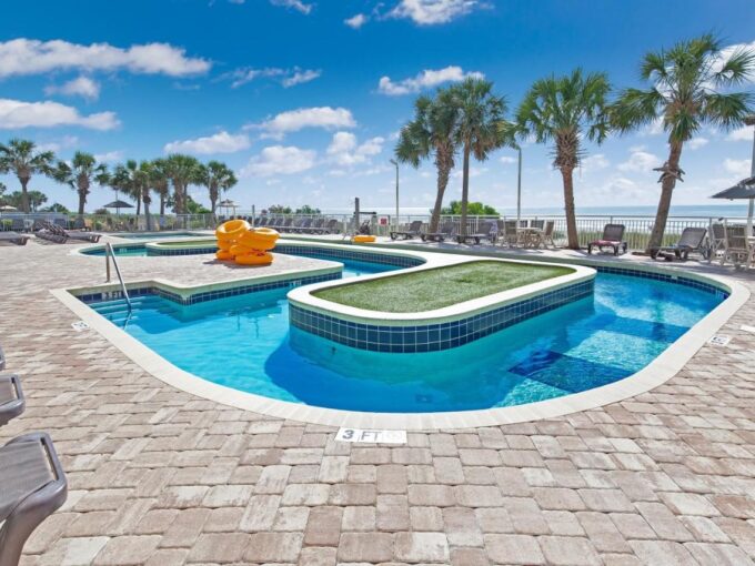 A pool with a yellow slide and some palm trees